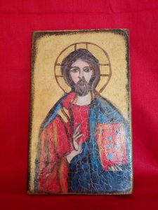 prostokątna ikona, na  bordowym tle przedstawiająca postać Jezusa, prawa dłoń uniesiona, w lewej księga