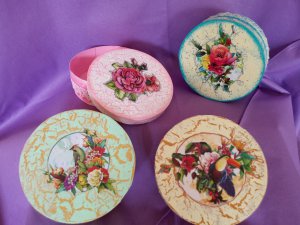 cztery okrągłe pudełka z wieczkami, jedno uchylone, na fioletowym tle, ozdobione metodą decoupage, roślinny ornament z dwoma ptakami